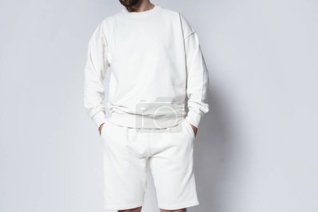 Foto de Hombre con sudadera blanca en blanco y pantalones cortos sobre fondo gris - Imagen libre de derechos