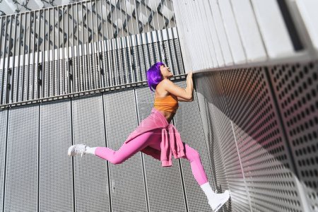 Téléchargez les photos : Heureuse femme active portant des vêtements de sport colorés grimpant sur le mur - en image libre de droit