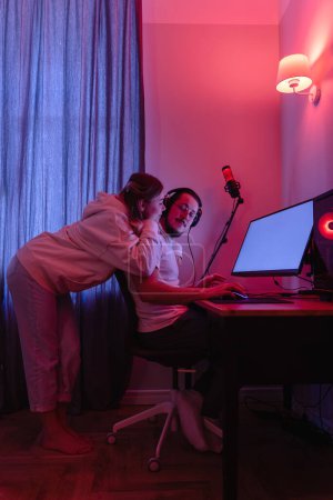 Téléchargez les photos : Jeune couple dans la chambre avec lumière au néon utilisent un ordinateur personnel moderne à la maison - en image libre de droit