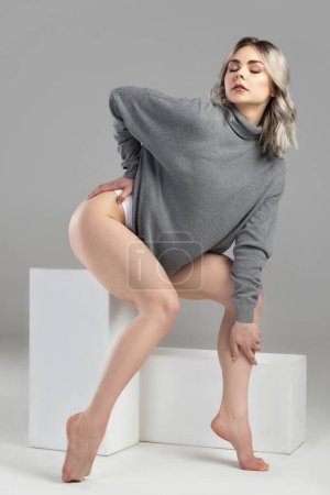 Photo for Portrait of young and sexy woman with blond hair wearing turtleneck jumper is posing on gray background in studio - Royalty Free Image
