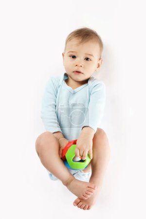 Téléchargez les photos : Adorable petit garçon dans une barboteuse est couché et jouer avec un jouet en plastique sur fond blanc. - en image libre de droit