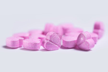 Nahaufnahme eines Haufens rosa Pillen in Herzform auf weißem Hintergrund.