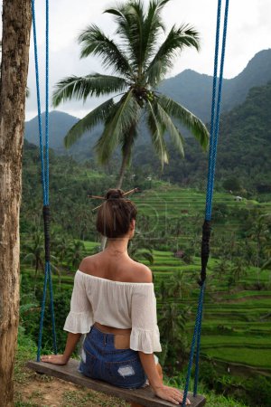 Foto de Mujer joven en columpios de cuerda con hermosa vista en terrazas de arroz en el Bali. - Imagen libre de derechos