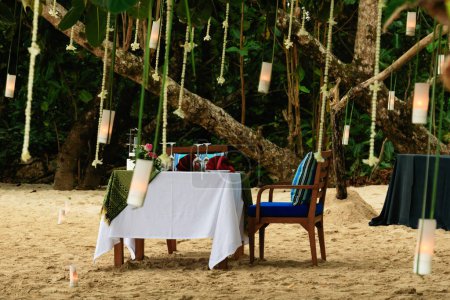 Foto de Mesa de comedor preparada para una cita romántica en una playa de arena, rodeada de velas. - Imagen libre de derechos