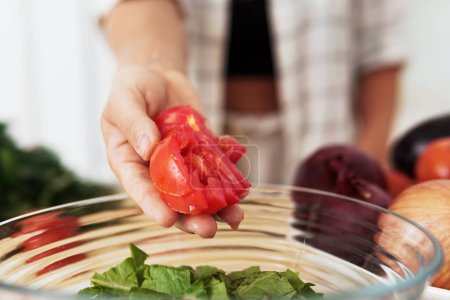 Photo for Closeup of female hand with sliced tomato and bowl with lettuce salad - Royalty Free Image