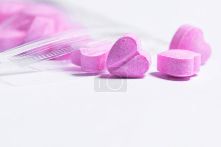 Photo for Closeup shot of a transparent ziplock bag and pink heart shaped pills on white background. - Royalty Free Image