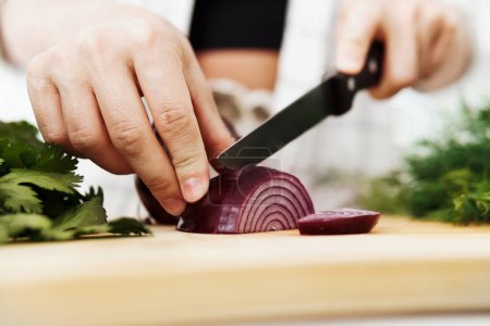 Téléchargez les photos : Gros plan de mains féminines avec couteau tranchant l'oignon rouge sur une planche à découper en bois - en image libre de droit