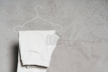 Photo for Mockup of blank white sweatpants hanging on the thin metallic hanger against light concrete wall - Royalty Free Image