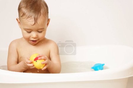 Photo for Adorable little boy is playing with a rubber duck while taking a bath in warm water. - Royalty Free Image