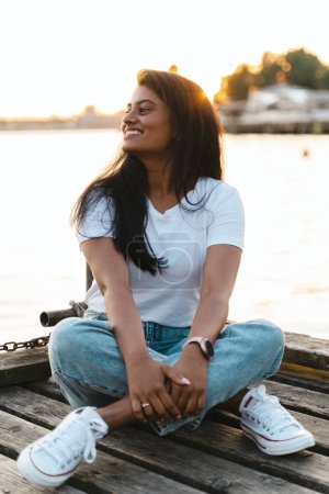 Photo for Carefree smiling Indian woman sitting on the wooden pier by the river - Royalty Free Image