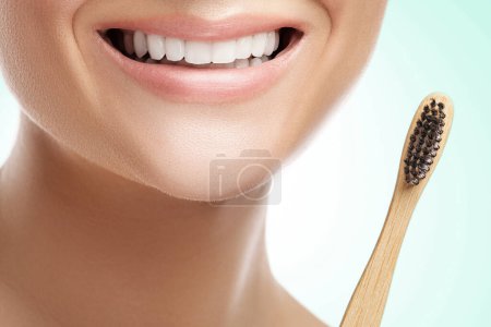 Foto de Boca femenina con dientes blancos y cepillo de dientes de bambú sobre fondo blanco - Imagen libre de derechos
