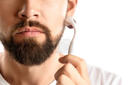 Foto de Hombre guapo usando rodillo meso para un mejor crecimiento de la barba sobre fondo blanco - Imagen libre de derechos