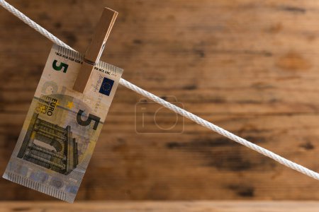 Téléchargez les photos : Cinq billets en euros séchent sur une corde blanche, tenue par une broche à linge. Compte d'épargne ou de blanchiment d'argent. - en image libre de droit
