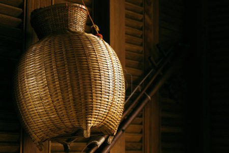 Foto de Primer plano de una cesta de mimbre de paja colgada en una pared de madera en una acogedora casa rural. - Imagen libre de derechos