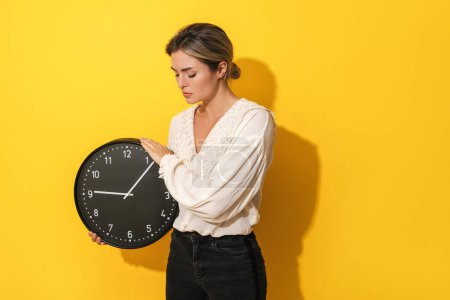 Photo for Upset young woman holding big clock on yellow background - Royalty Free Image