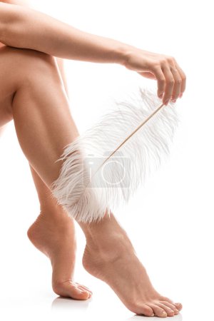 Photo for Closeup of female feet with smooth skin and soft ostrich feather on white background - Royalty Free Image