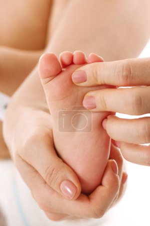 Photo for Closeup shot of a mother gently massaging her little child's feet and soles on white background. - Royalty Free Image