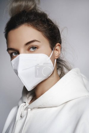 Téléchargez les photos : Jeune femme portant capuche blanche et masque respirateur ffp2 sur fond gris - en image libre de droit