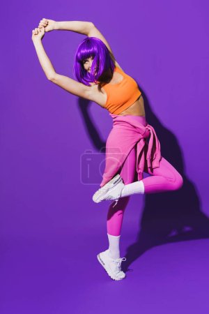Foto de Bailarina joven despreocupada vistiendo ropa deportiva colorida actuando sobre fondo púrpura - Imagen libre de derechos