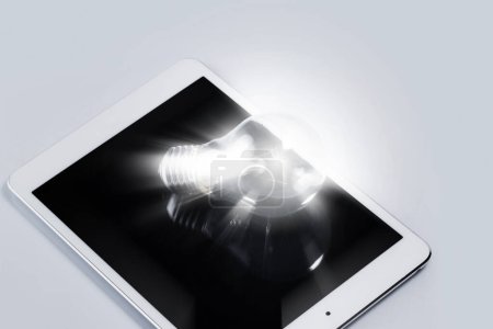 Photo for Closeup of light bulb lying on white tablet computer. Concept of innovation and solutions in business. - Royalty Free Image