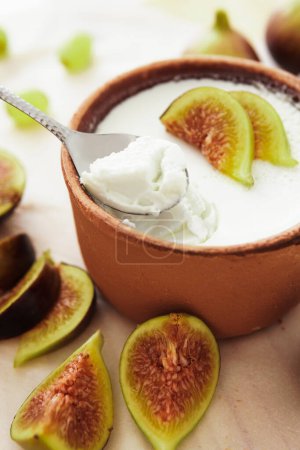 Foto de Primer plano de cuchara y delicioso yogur griego natural en tazón de barro con higos - Imagen libre de derechos