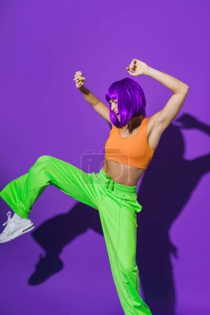Foto de Bailarina activa despreocupada que usa ropa deportiva colorida que se divierte contra el fondo púrpura - Imagen libre de derechos