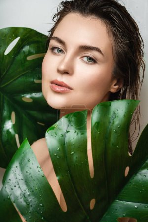 Téléchargez les photos : Portrait de belle jeune femme à la peau lisse tenant Monstera deliciosa feuille de plante - en image libre de droit