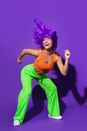 Photo for Carefree active woman dancer wearing colorful sportswear having fun against purple background - Royalty Free Image