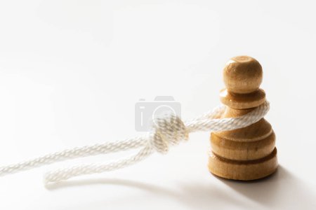 Photo for Closeup shot of white rope tangled around a wooden chess pawn. Concept of facing difficulties in life and being burdened by responsibility. - Royalty Free Image