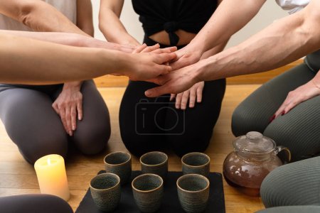 Photo for Young women friends kneeling around the tray are putting hands together during tea ceremony. - Royalty Free Image