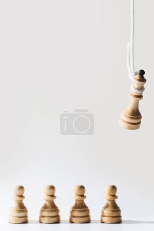 Foto de Primer plano de una reina de ajedrez de madera colgada en una cuerda blanca con peones de pie debajo. Concepto de enfrentarse a la desaprobación del público y ser agobiado por la responsabilidad. - Imagen libre de derechos