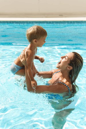 Foto de Feliz madre y su lindo hijo nadando en la piscina al aire libre durante las vacaciones de verano - Imagen libre de derechos