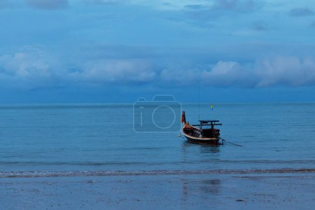 Téléchargez les photos : Beau paysage avec un bateau de pêche flottant dans la mer calme près de la plage de sable avec ciel nuageux en soirée en arrière-plan. - en image libre de droit