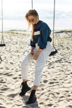 Foto de Joven mujer bonita está sentada en el columpio y sonriendo en la playa de arena. - Imagen libre de derechos
