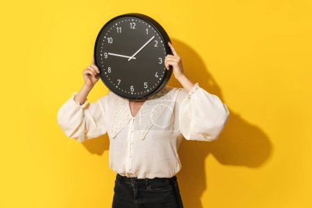 Photo for Time management concept. Woman covering her face with big clock on yellow background. - Royalty Free Image