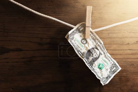 Téléchargez les photos : Un billet d'un dollar sèche sur une corde blanche, tenue par une épingle à linge. Compte d'épargne ou de blanchiment d'argent. - en image libre de droit