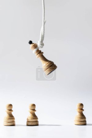 Photo for Closeup shot of a wooden chess queen hanging on a white rope with pawns standing below. Concept of facing public disapproval and being burdened by responsibility. - Royalty Free Image