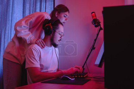 Téléchargez les photos : Jeune couple dans la chambre avec lumière au néon utilisent un ordinateur personnel moderne à la maison - en image libre de droit