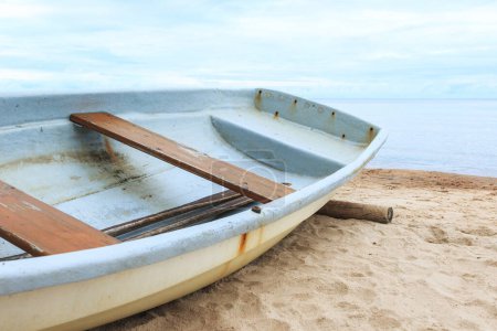 Photo for Closeup shot of a abandoned shabby fishing boat lying on a sandy beach near the calm sea water. - Royalty Free Image