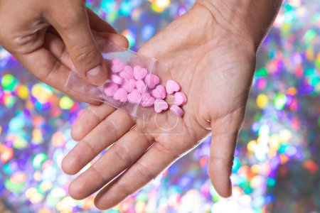Nahaufnahme eines Mannes, der rosafarbene Pillen in Herzform aus einer transparenten Reißverschlusstasche auf hellem, verschwommenem Hintergrund auf die Handfläche schüttet.
