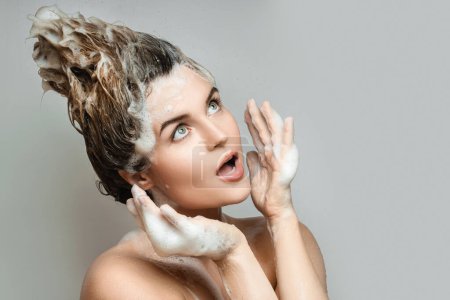 Portrait of young and funny woman is washing her hair with a shampoo