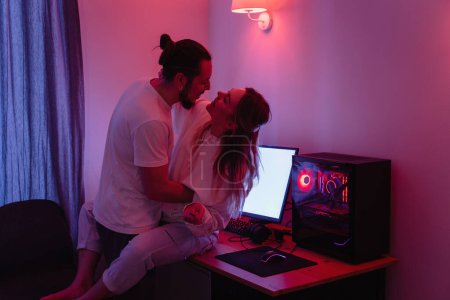 Foto de Joven pareja alegre en la habitación con luz de neón, divertirse en la mesa con el juego de ordenador personal en casa - Imagen libre de derechos