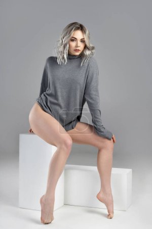 Photo for Portrait of young and sexy woman with blond hair wearing turtleneck jumper is posing on gray background in studio - Royalty Free Image