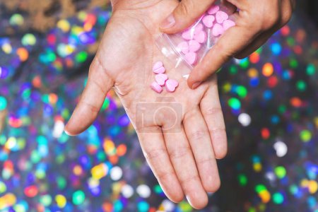 Photo for Closeup shot of a man pouring pink heart shaped pills on its palm from a transparent ziplock bag on bright blurry background. - Royalty Free Image