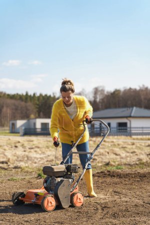 Photo for Young woman villager is using aerator machine to scarification and aeration of lawn or meadow - Royalty Free Image