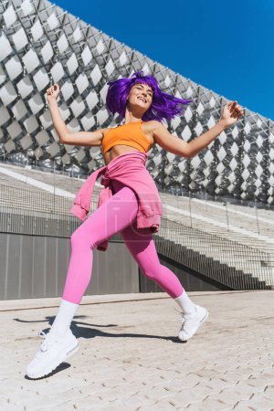 Téléchargez les photos : Femme active insouciante danseuse portant des vêtements de sport colorés s'amusant dans la rue pendant la journée ensoleillée - en image libre de droit