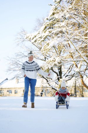 Téléchargez les photos : Mère et son mignon petit fils portant des pulls chauds ont sur une colline de luge pendant la journée ensoleillée d'hiver - en image libre de droit