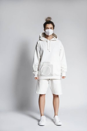 Photo for Young woman wearing white hoodie and ffp2 respirator mask against gray background - Royalty Free Image