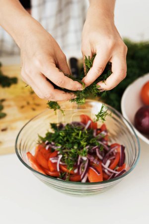 Téléchargez les photos : Gros plan de mains féminines cuisine salade végétarienne et y ajoutant de l'aneth vert - en image libre de droit