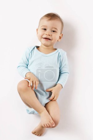 Foto de Adorable niño en un mameluco está acostado boca arriba y sonriendo sobre fondo blanco. - Imagen libre de derechos